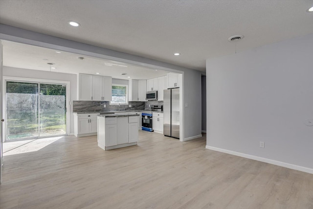 kitchen with a kitchen island, tasteful backsplash, light hardwood / wood-style floors, white cabinetry, and stainless steel appliances