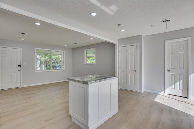 kitchen with a center island, white cabinets, light hardwood / wood-style flooring, a textured ceiling, and light stone counters