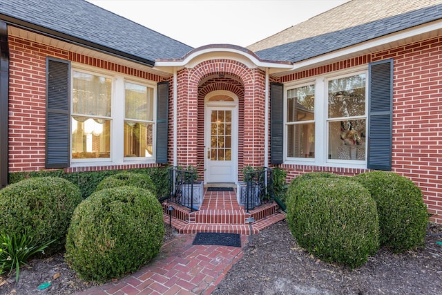 doorway to property featuring roof with shingles and brick siding