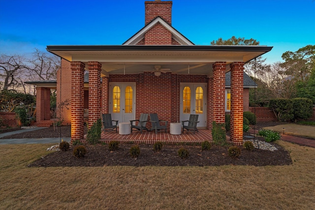 back of property with french doors, brick siding, a lawn, and a chimney