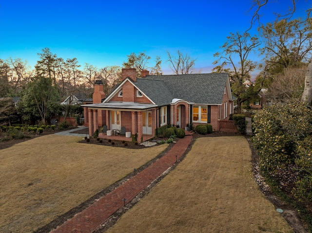 view of front of home featuring brick siding, roof with shingles, a chimney, driveway, and a front lawn