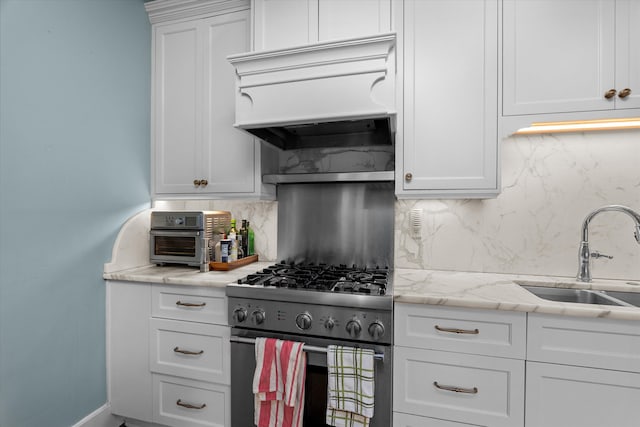 kitchen featuring decorative backsplash, high end stainless steel range, custom exhaust hood, white cabinetry, and a sink