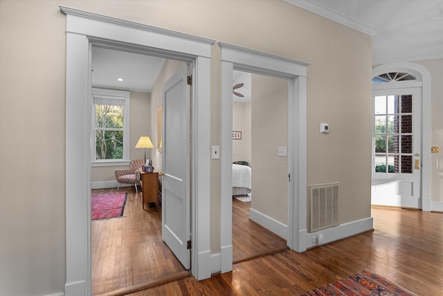 hall featuring baseboards, hardwood / wood-style flooring, visible vents, and crown molding