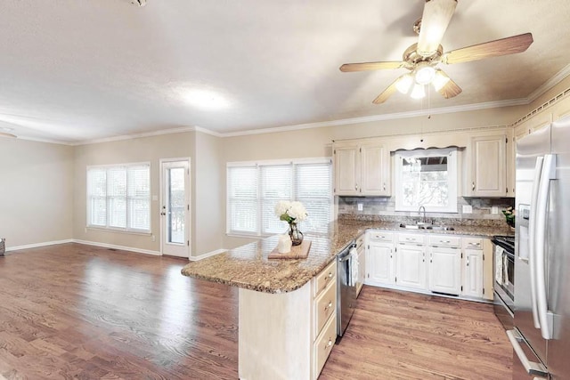 kitchen with appliances with stainless steel finishes, sink, backsplash, light stone counters, and light hardwood / wood-style floors