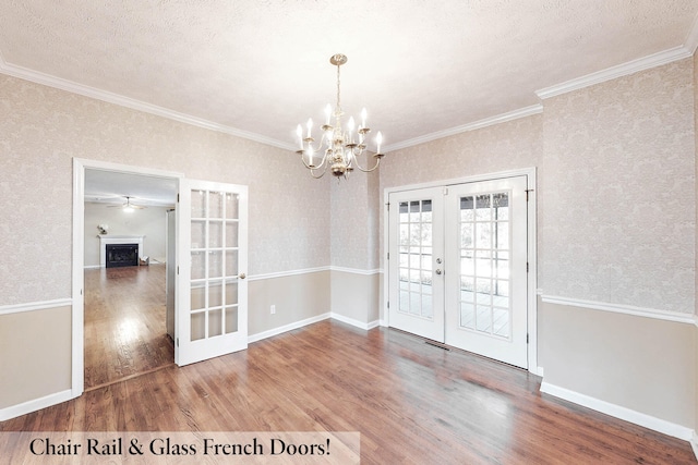 unfurnished dining area featuring french doors, crown molding, a textured ceiling, a notable chandelier, and hardwood / wood-style flooring