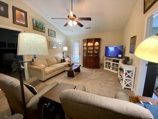 living room with lofted ceiling, visible vents, carpet floors, and a ceiling fan