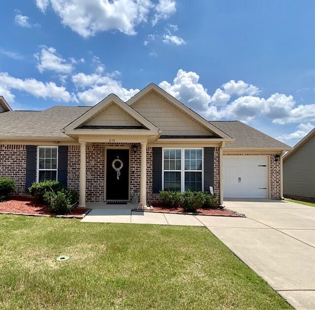 view of front of house with brick siding, roof with shingles, a front yard, a garage, and driveway