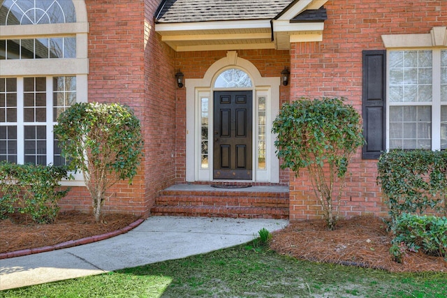 doorway to property with a shingled roof and brick siding