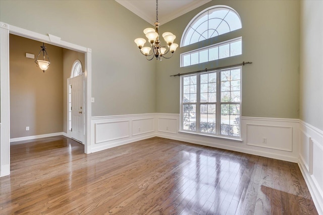 unfurnished dining area featuring a chandelier, a decorative wall, a wainscoted wall, wood finished floors, and vaulted ceiling