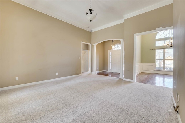 empty room featuring arched walkways, carpet floors, a towering ceiling, ornamental molding, and decorative columns