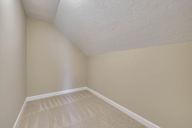 additional living space featuring carpet, vaulted ceiling, a textured ceiling, and baseboards