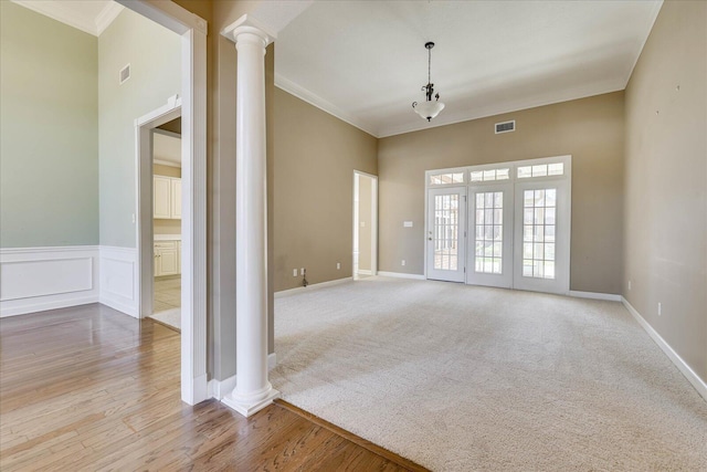 empty room featuring ornate columns, wainscoting, visible vents, and ornamental molding