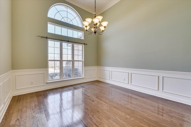 empty room with a wainscoted wall, crown molding, wood finished floors, and a notable chandelier