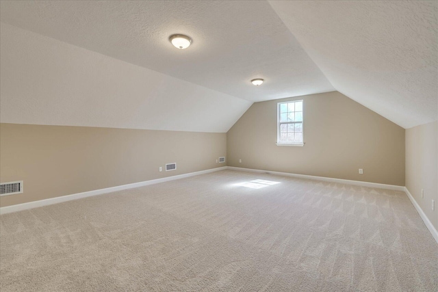 bonus room with light carpet, visible vents, and a textured ceiling