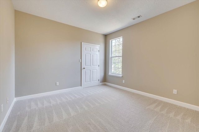 spare room featuring visible vents, light carpet, a textured ceiling, and baseboards