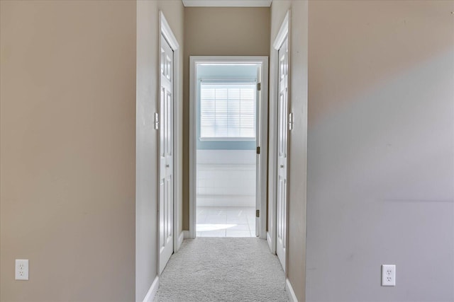 hallway featuring light colored carpet and baseboards