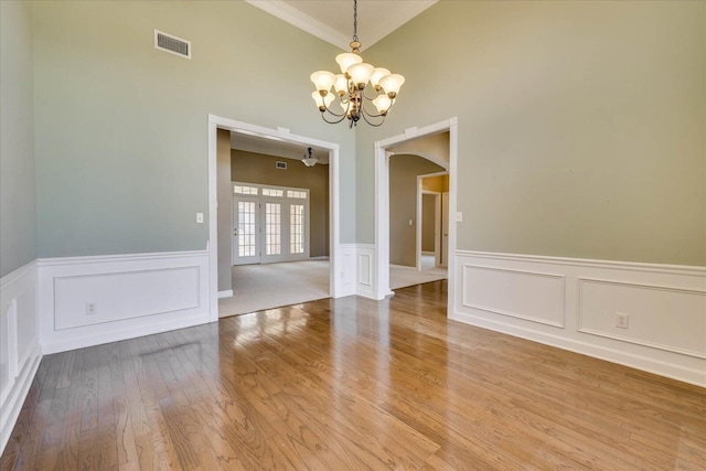 unfurnished dining area with a wainscoted wall, wood finished floors, visible vents, and a notable chandelier