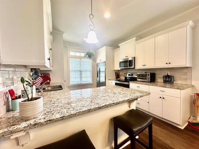 kitchen with pendant lighting, a breakfast bar, white cabinets, dark hardwood / wood-style floors, and appliances with stainless steel finishes