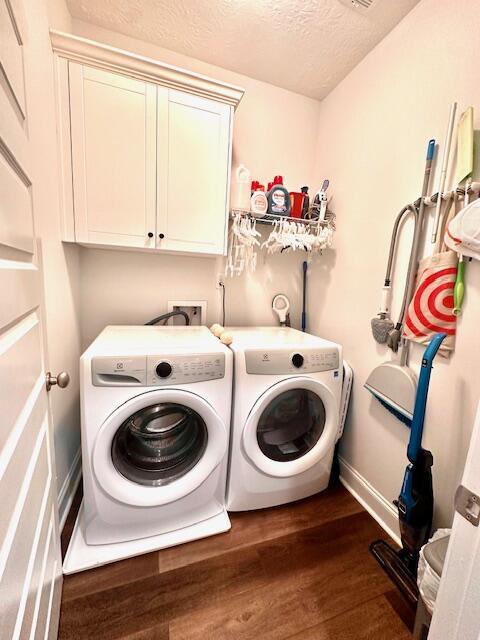 laundry area with cabinets, a textured ceiling, washing machine and dryer, and dark hardwood / wood-style floors