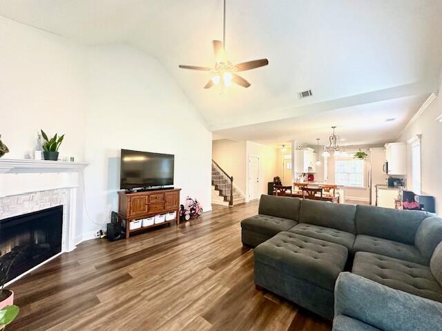 living room with vaulted ceiling, a stone fireplace, hardwood / wood-style floors, and ceiling fan with notable chandelier