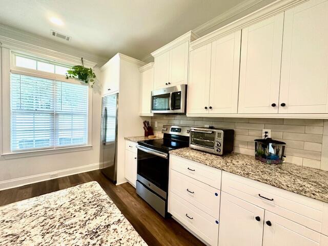 kitchen featuring dark hardwood / wood-style floors, light stone countertops, appliances with stainless steel finishes, tasteful backsplash, and white cabinetry