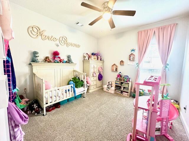 carpeted bedroom featuring a nursery area and ceiling fan