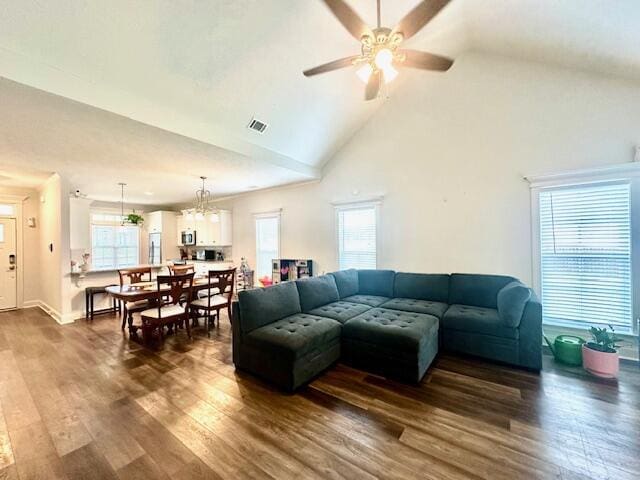 living room with a healthy amount of sunlight, high vaulted ceiling, dark wood-type flooring, and ceiling fan with notable chandelier