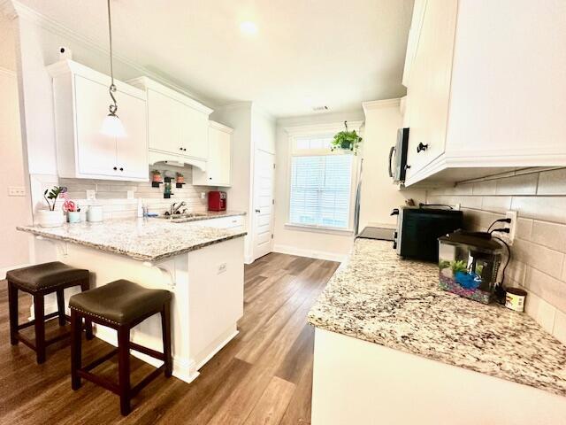 kitchen featuring light stone counters, dark wood-type flooring, pendant lighting, white cabinets, and a breakfast bar area