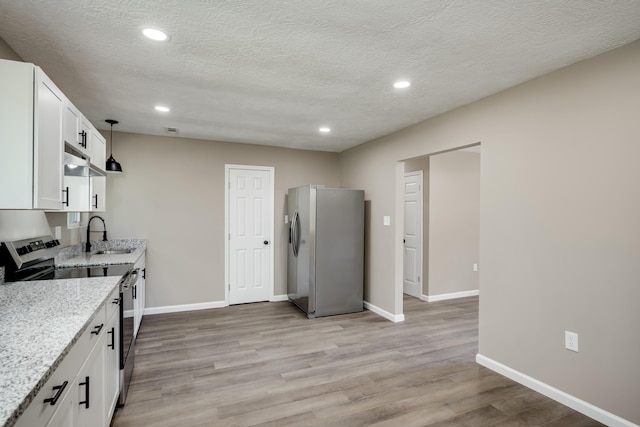 kitchen with light stone counters, stainless steel appliances, white cabinets, a sink, and light wood-type flooring