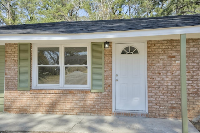 property entrance featuring brick siding and a shingled roof