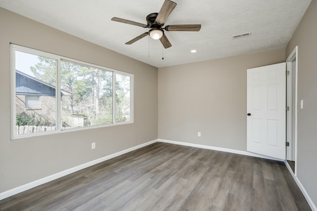 unfurnished room with a textured ceiling, wood finished floors, a ceiling fan, visible vents, and baseboards