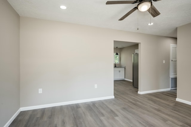 spare room with a textured ceiling, wood finished floors, visible vents, a ceiling fan, and baseboards