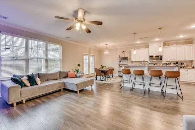 living room featuring ceiling fan, ornamental molding, and light hardwood / wood-style floors