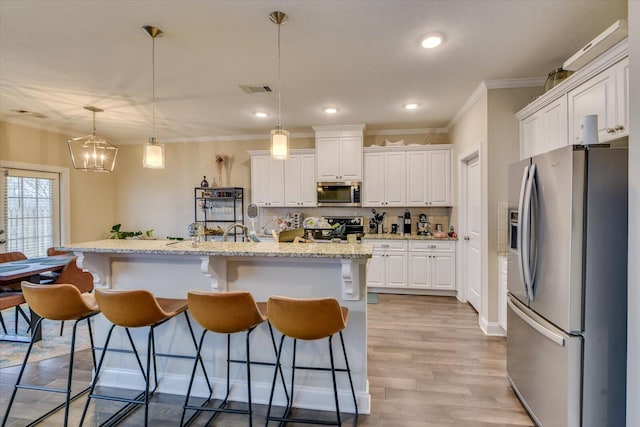 kitchen with pendant lighting, stainless steel appliances, a center island with sink, and white cabinets