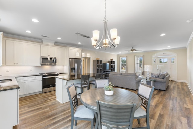 dining space featuring hardwood / wood-style flooring, crown molding, ceiling fan with notable chandelier, and sink