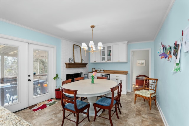 dining room with a notable chandelier, crown molding, french doors, and a brick fireplace