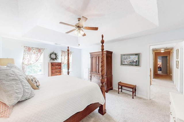 bedroom with a raised ceiling, baseboards, light carpet, and a ceiling fan