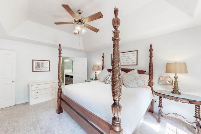 carpeted bedroom with baseboards, a tray ceiling, ceiling fan, and ensuite bathroom