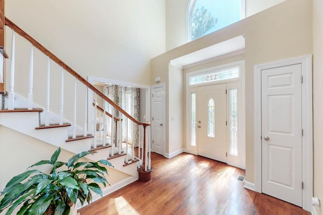 entryway with baseboards, wood finished floors, a towering ceiling, visible vents, and stairway