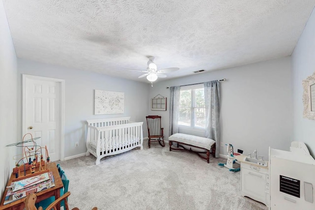 carpeted bedroom with baseboards, a textured ceiling, a crib, and ceiling fan