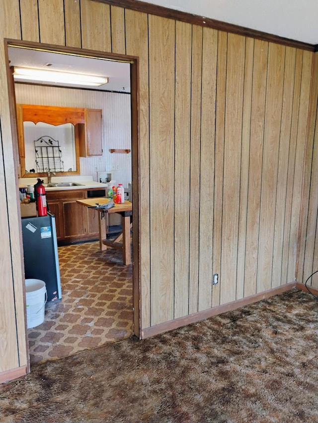 kitchen featuring crown molding, dark carpet, wooden walls, and sink