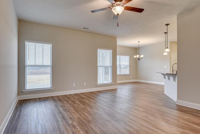 kitchen with light stone countertops, stainless steel appliances, a center island with sink, white cabinets, and ceiling fan with notable chandelier