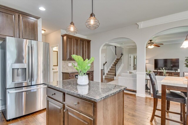 kitchen featuring pendant lighting, stainless steel refrigerator with ice dispenser, decorative backsplash, stone countertops, and a kitchen island