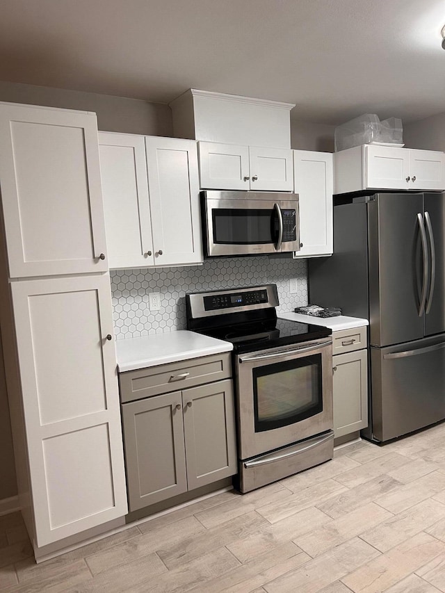 kitchen featuring white cabinets, light wood-type flooring, stainless steel appliances, and tasteful backsplash