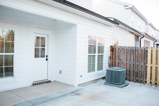 view of exterior entry with a patio area, fence, and central air condition unit