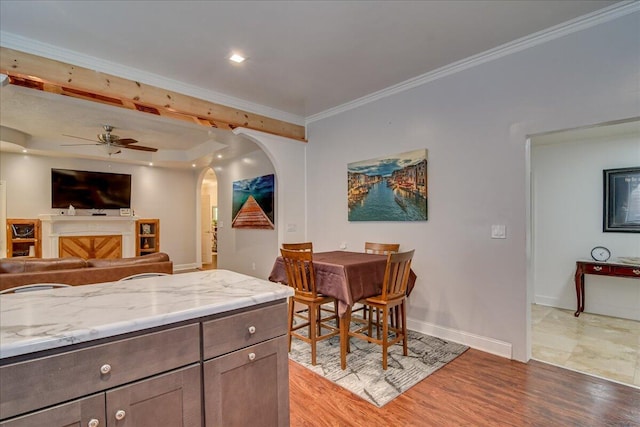 kitchen featuring ceiling fan, light stone counters, light wood-type flooring, and crown molding