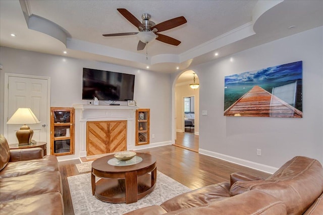 living room with wood-type flooring, a raised ceiling, and ceiling fan