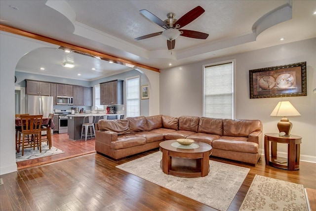 living room featuring ceiling fan, light wood-type flooring, ornamental molding, and a tray ceiling