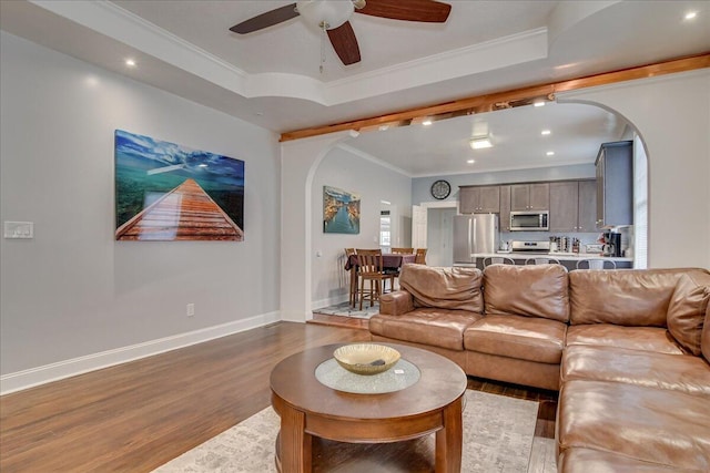 living room featuring hardwood / wood-style flooring, ceiling fan, ornamental molding, and a tray ceiling