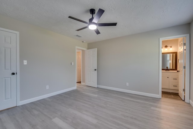 unfurnished bedroom featuring visible vents, a textured ceiling, ensuite bath, light wood-type flooring, and baseboards